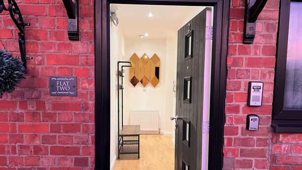 A hotel entrance with a brick wall, a sign reading "FLAT TWO", and a door with a keypad lock. - Lux Modern Apartment in Nuneaton (Nuneaton)