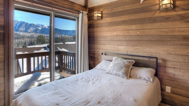 A bedroom with a large window, wooden walls, and a bed with white bedding.