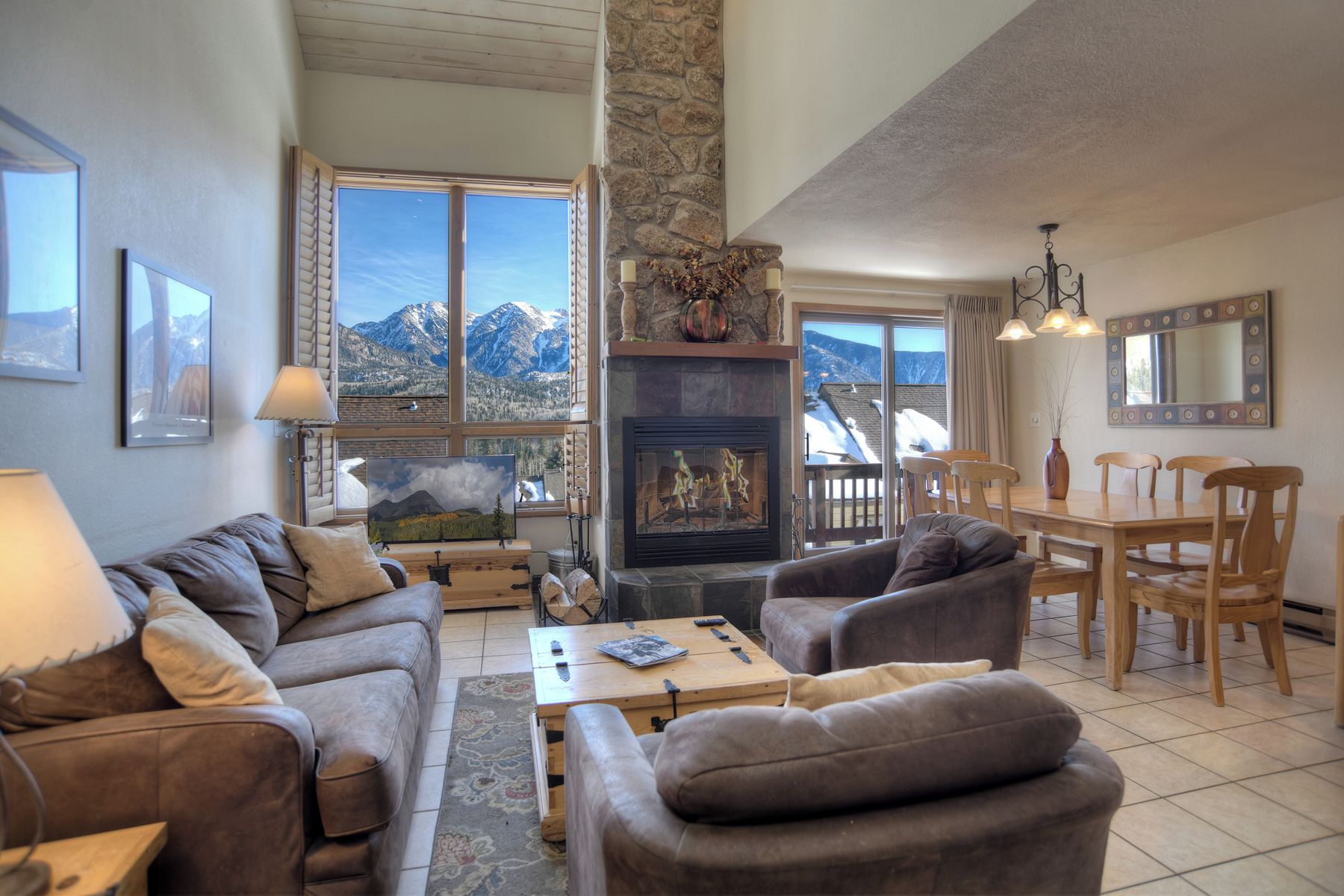 A cozy living room with a fireplace, a dining area, and large windows offering mountain views.