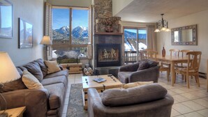 A cozy living room with a fireplace, a dining area, and large windows offering mountain views.