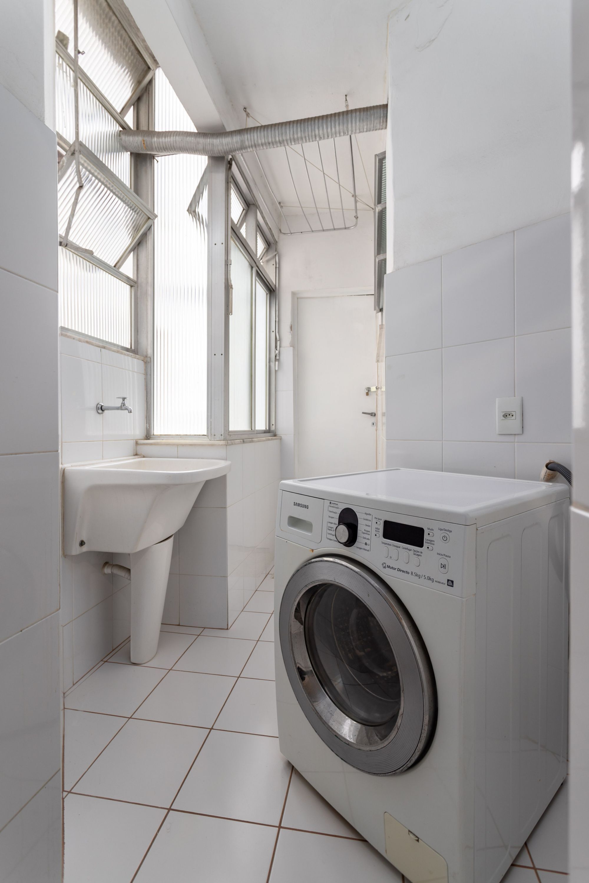 Ein Waschraum mit einer Frontlader-Waschmaschine, einem Waschbecken und einem Fenster mit Jalousien.