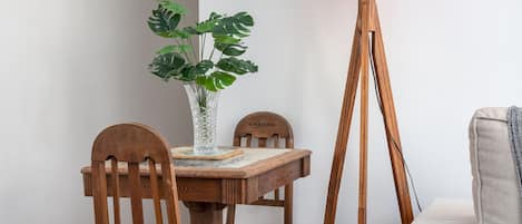 A dining area with a wooden table, chairs, a vase with green plants, and a floor lamp with a red shade.