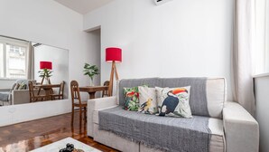 A living room with a grey sofa, a red floor lamp, and a table with fruit.