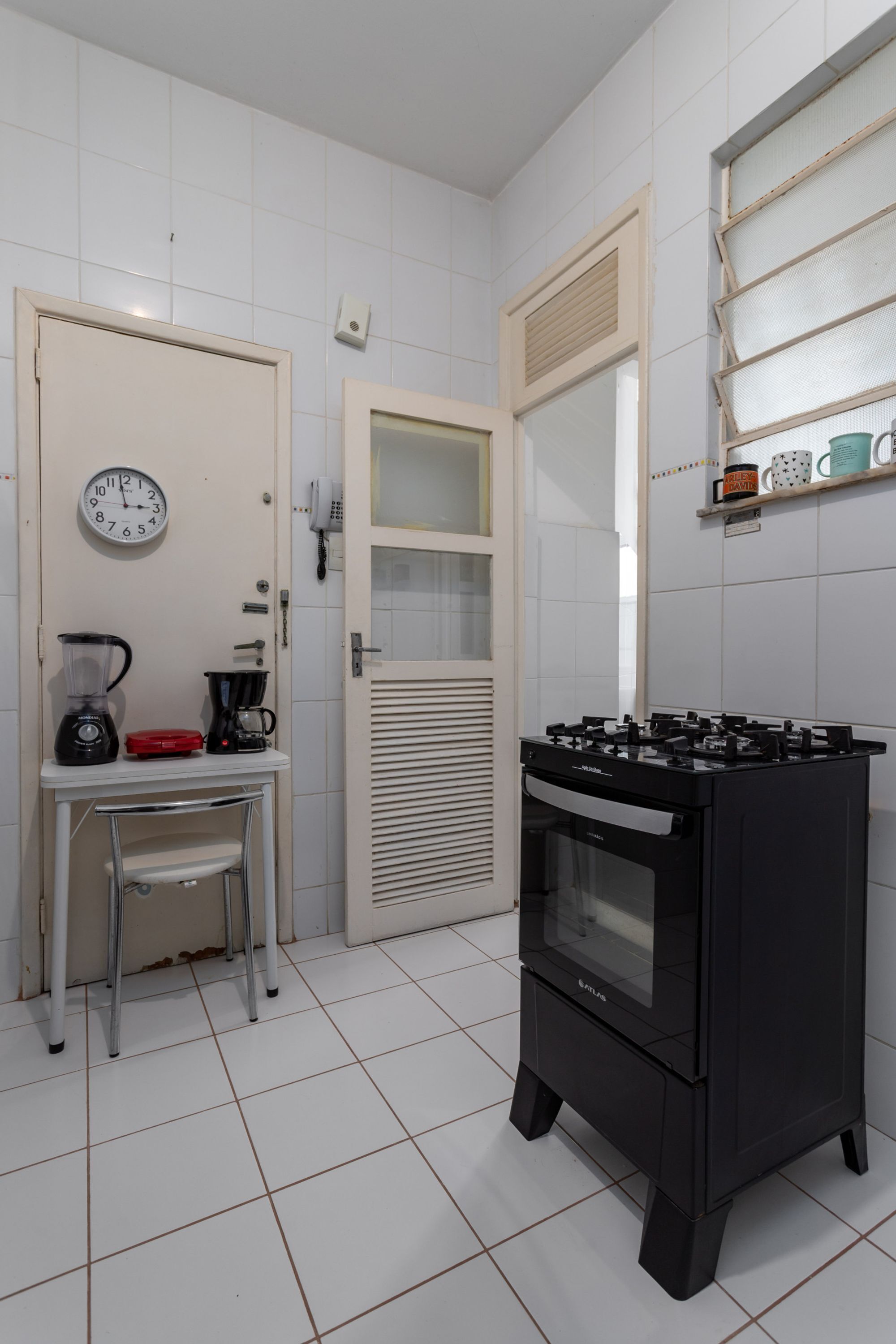 A kitchen with a stove, a coffee maker, a blender, and a clock on the wall.