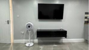A room with a flat-screen TV mounted on the wall, a white standing fan, and a black console table. - Place to stay in Erith (Erith)