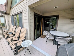 A covered outdoor seating area with wooden chairs and a round table, a sliding glass door, and a small white table.