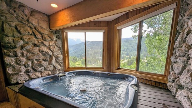 Ein Whirlpool in einem Raum mit Steinwänden und großen Fenstern mit Blick auf einen bewaldeten Bereich.