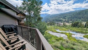 Ein Balkon mit Holzstühlen mit Blick auf einen Fluss und bewaldete Berge.
