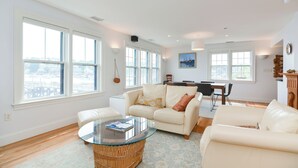 A spacious living room with large windows, a glass coffee table, and a dining area with a table and chairs.