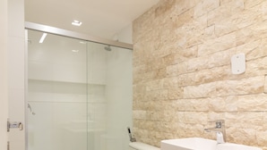 A modern bathroom with a glass shower enclosure, a white sink, and wooden cabinets. - Comfort in Leblon 10 Minutes From the Beach Bm802 (Rio de Janeiro)