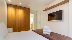 A hotel room with a large bed, a wooden wardrobe, a flat-screen TV mounted on the wall, and a bathroom visible through an open door. - Comfort in Leblon 10 Minutes From the Beach Bm802 (Rio de Janeiro)