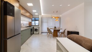 A modern kitchen with a built-in dishwasher, a dining area with a round table and chairs, and a large window providing natural light. - Comfort in Leblon 10 Minutes From the Beach Bm802 (Rio de Janeiro)