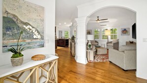 A spacious living area with a wooden floor, a white sofa, a coffee table, and a painting on the wall. - Poipu golf course villa with private lanai and fire pit summer deals (Koloa)