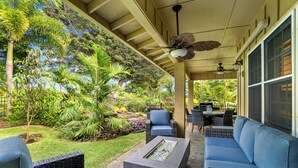 A covered outdoor seating area with wicker furniture, a fire feature, and lush tropical vegetation. - Poipu golf course villa with private lanai and fire pit summer deals (Koloa)