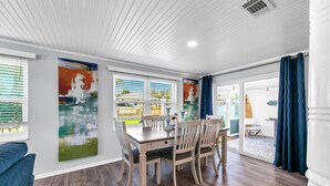 A dining area with a wooden table and chairs, large windows with blinds, and artwork on the walls. - 🏖️Walk to Beach-Great Location-A Wave We Go🏖️ (Panama City Beach)