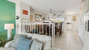 Una sala de estar moderna con un sofá, una zona de comedor con mesa y sillas, y una cocina al fondo.