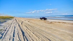 Una playa arenosa con surcos de neumáticos y un vehículo.