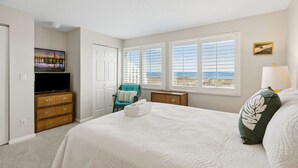 Un dormitorio con una cama grande, televisión, una silla y vistas a la playa.
