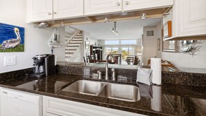 Una cocina con gabinetes blancos, encimera de granito, cafetera y lavabo.