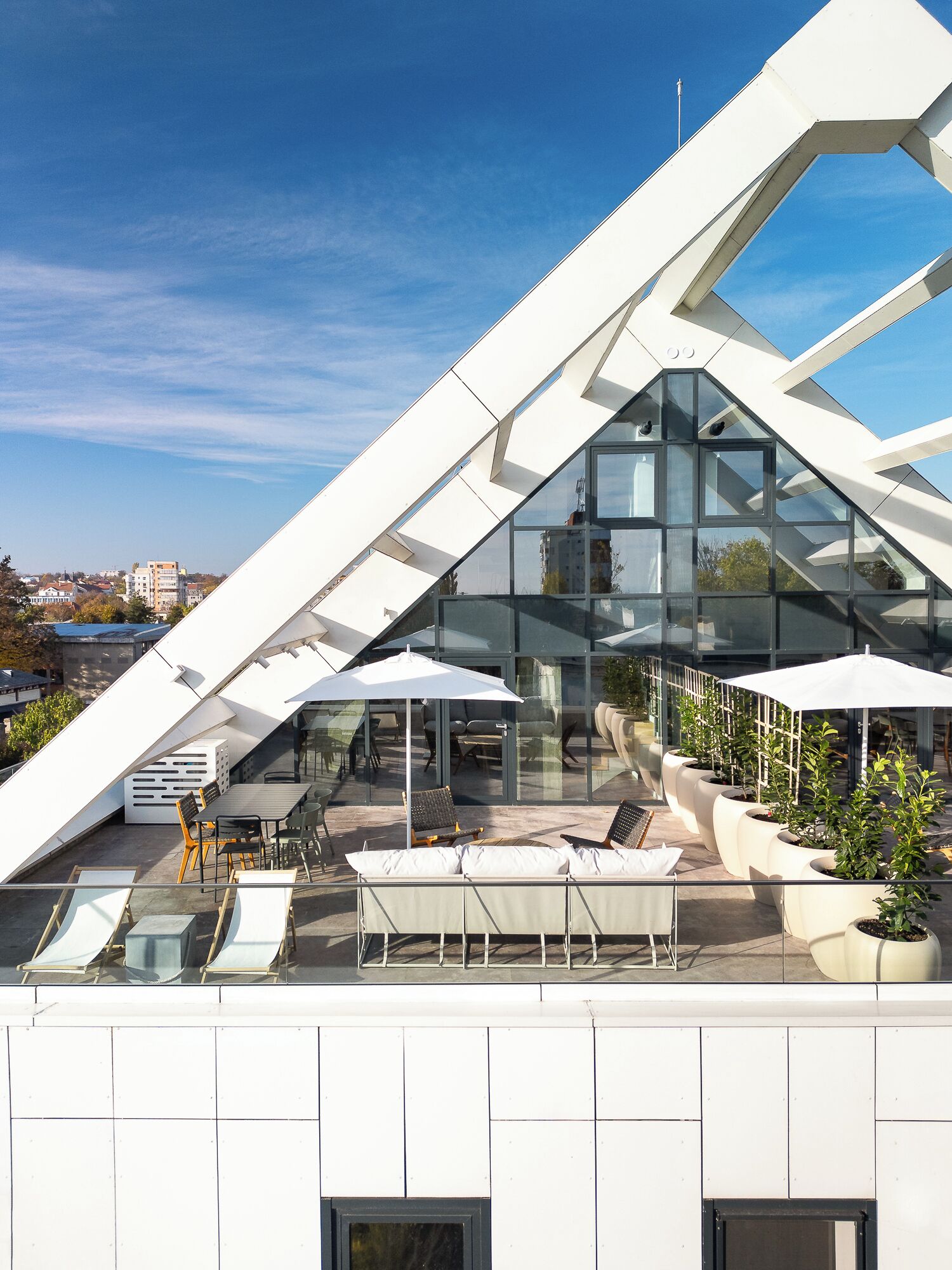 Une terrasse moderne sur le toit, dotée de murs en verre, d’un espace salon extérieur et de plantes en pot.