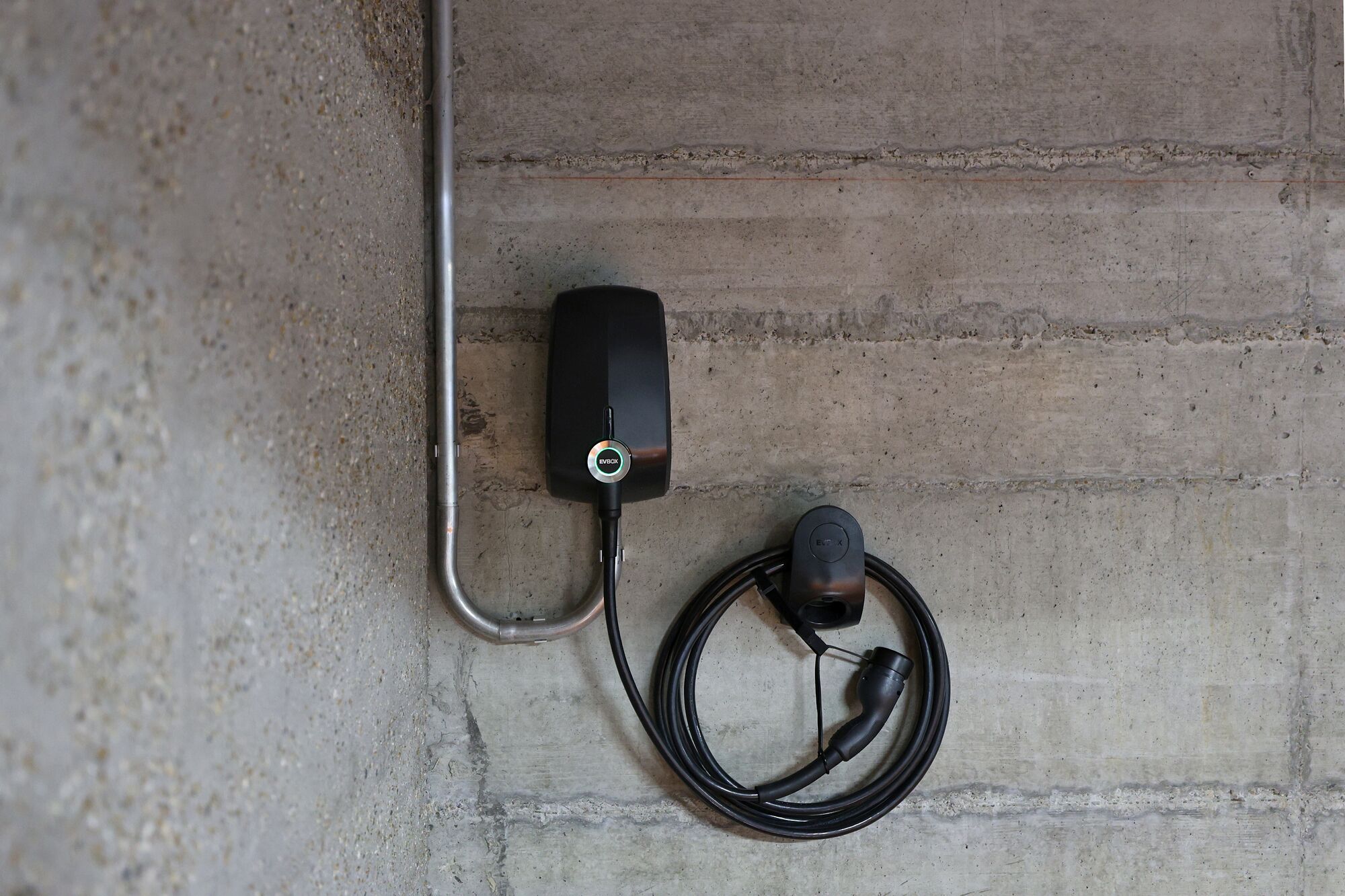 Une borne de recharge EVBOX fixée au mur, avec un câble branché à une prise de courant.