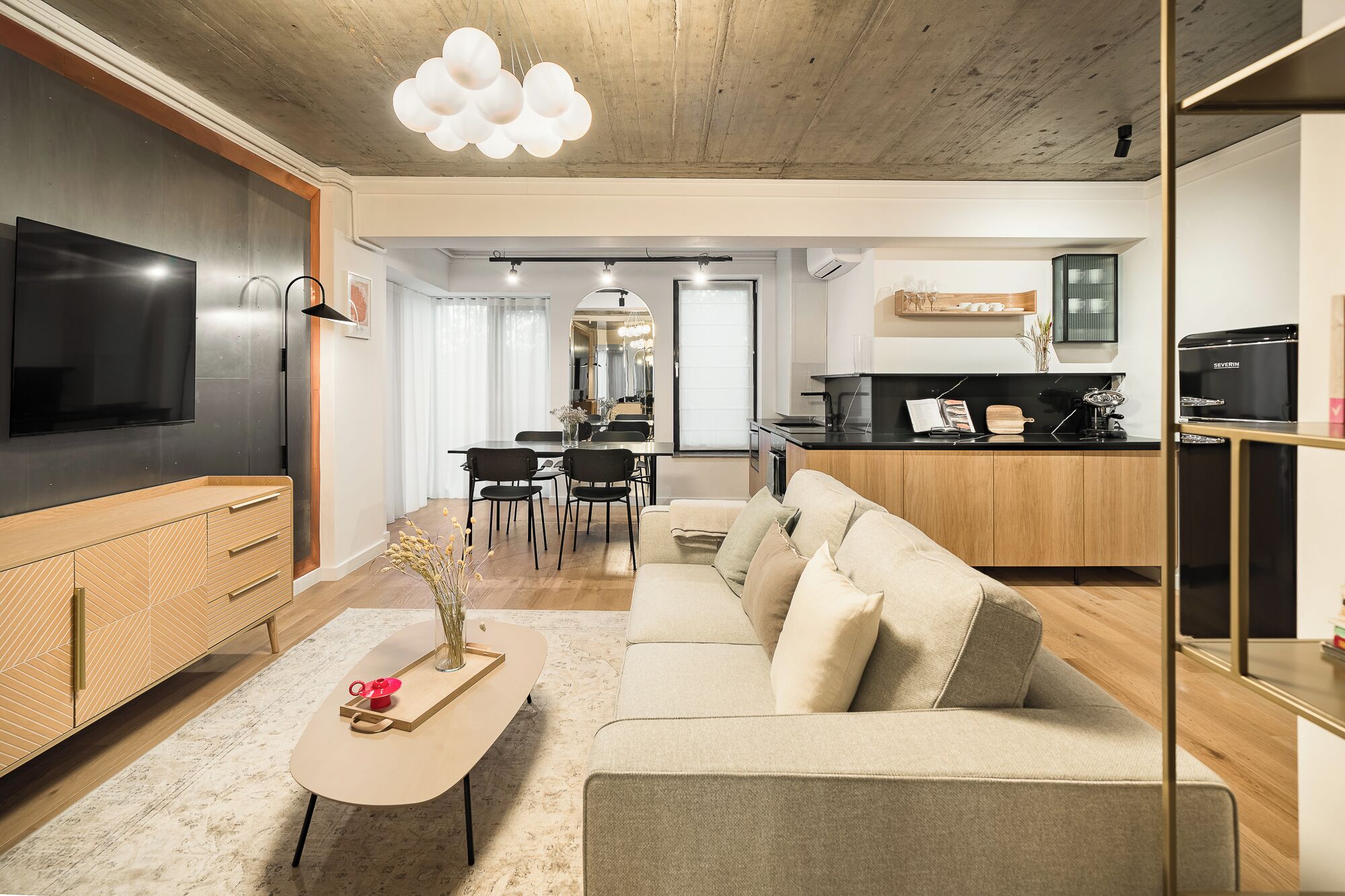 Una sala de estar moderna con sofá, mesa de centro y televisor. Hay una zona de cocina con mesa y sillas para comer.