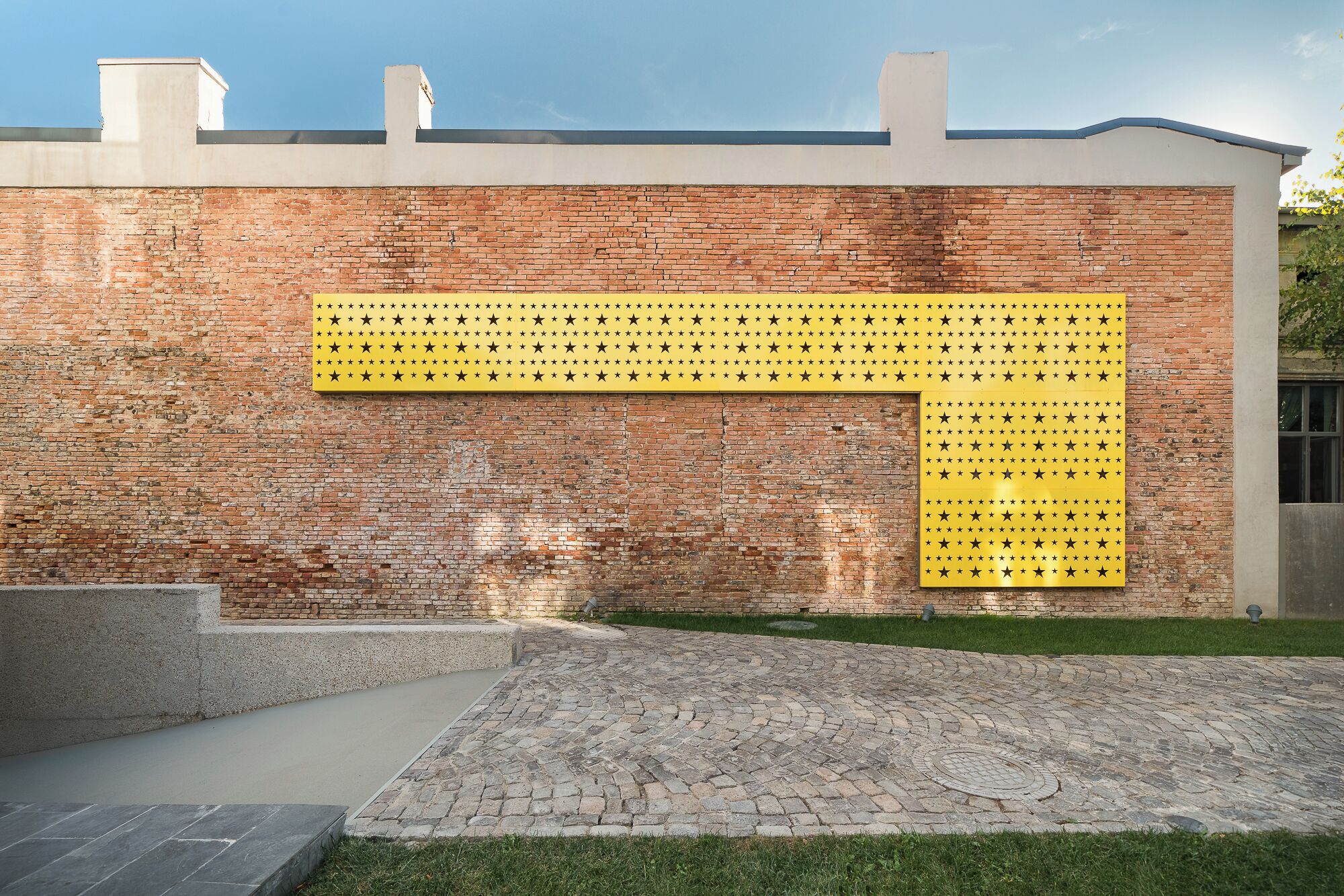 Un mur de briques avec un panneau jaune orné d’étoiles noires.