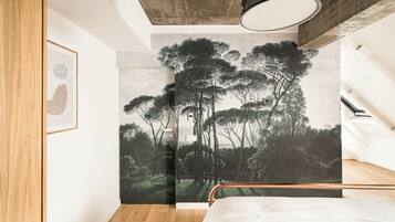 A bedroom with a bed, a wooden wardrobe, a ceiling light, and a wall mural of trees.