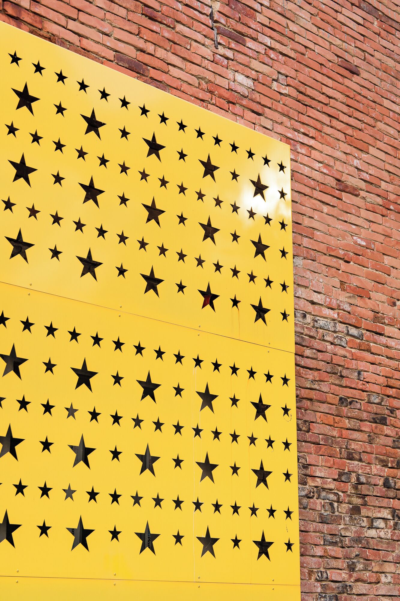 Un panel amarillo con estrellas negras sobre un muro de ladrillo.