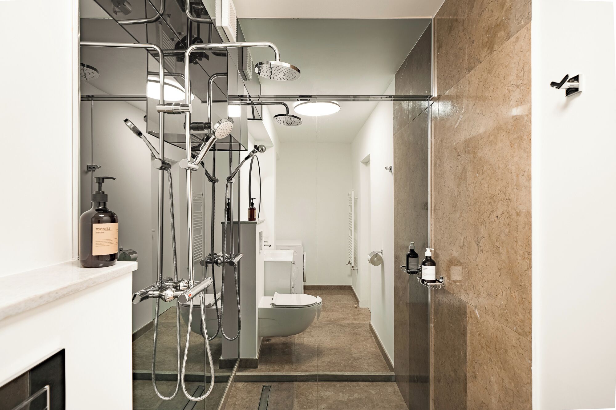 Un baño moderno con cabina de ducha de vidrio, inodoro y lavamanos con una botella de jabón corporal Meraki.