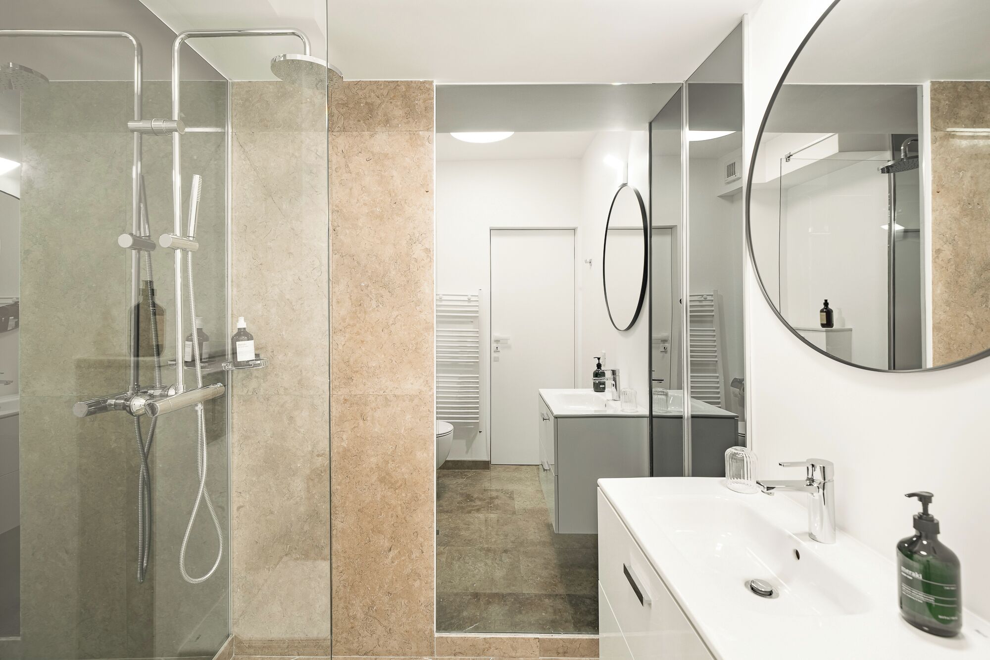 A modern bathroom with a glass-enclosed shower, a white sink with a mirror, and a towel rack.