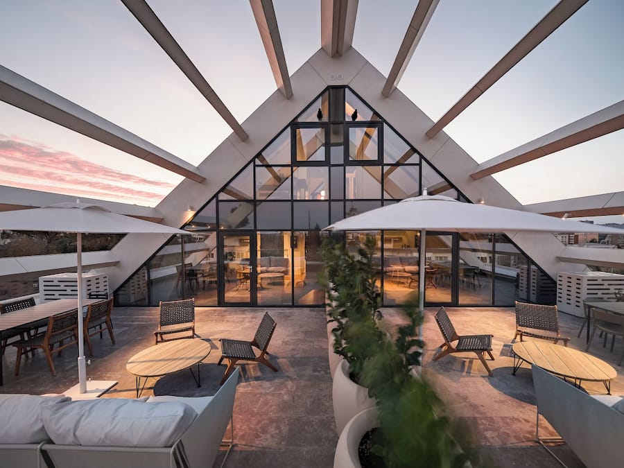 A modern rooftop terrace with glass walls, outdoor seating, and a view of the cityscape.