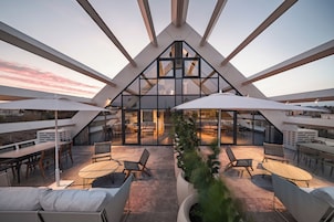 Una terraza moderna en la azotea con paredes de vidrio, asientos exteriores y vistas a la ciudad.
