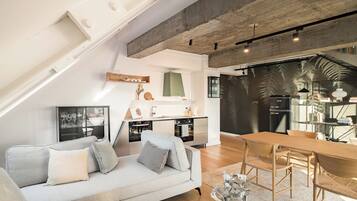 Un apartamento loft moderno con cama de altillo, kitchenette, comedor y sala de estar con sofá y sillones.