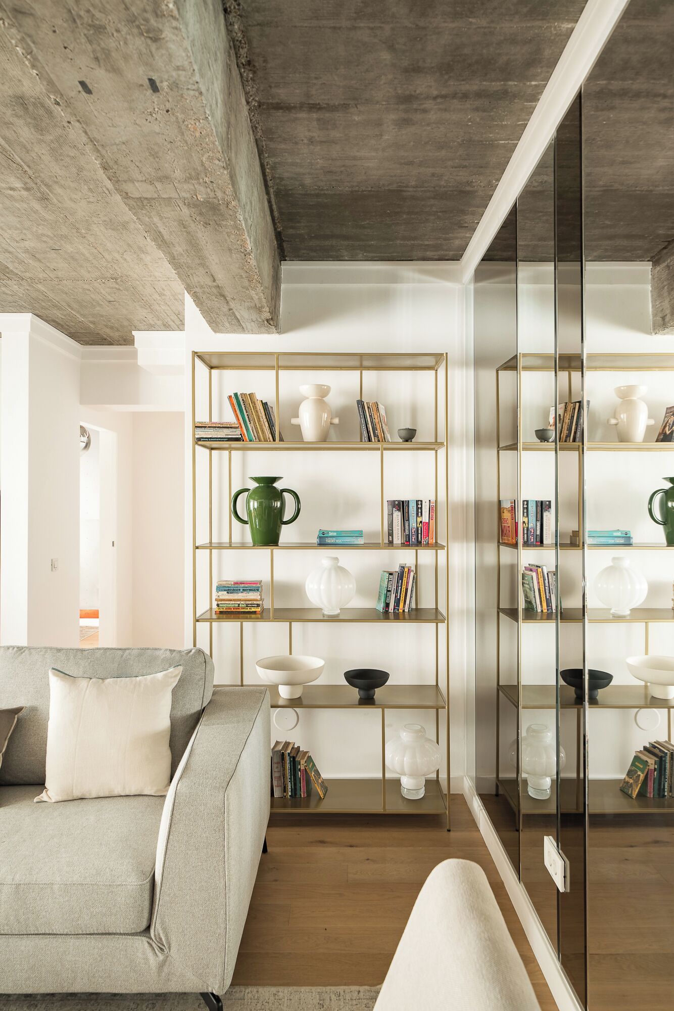 Een moderne woonkamer met een grijze bank, een houten salontafel en een boekenkast met diverse decoratieve objecten.
