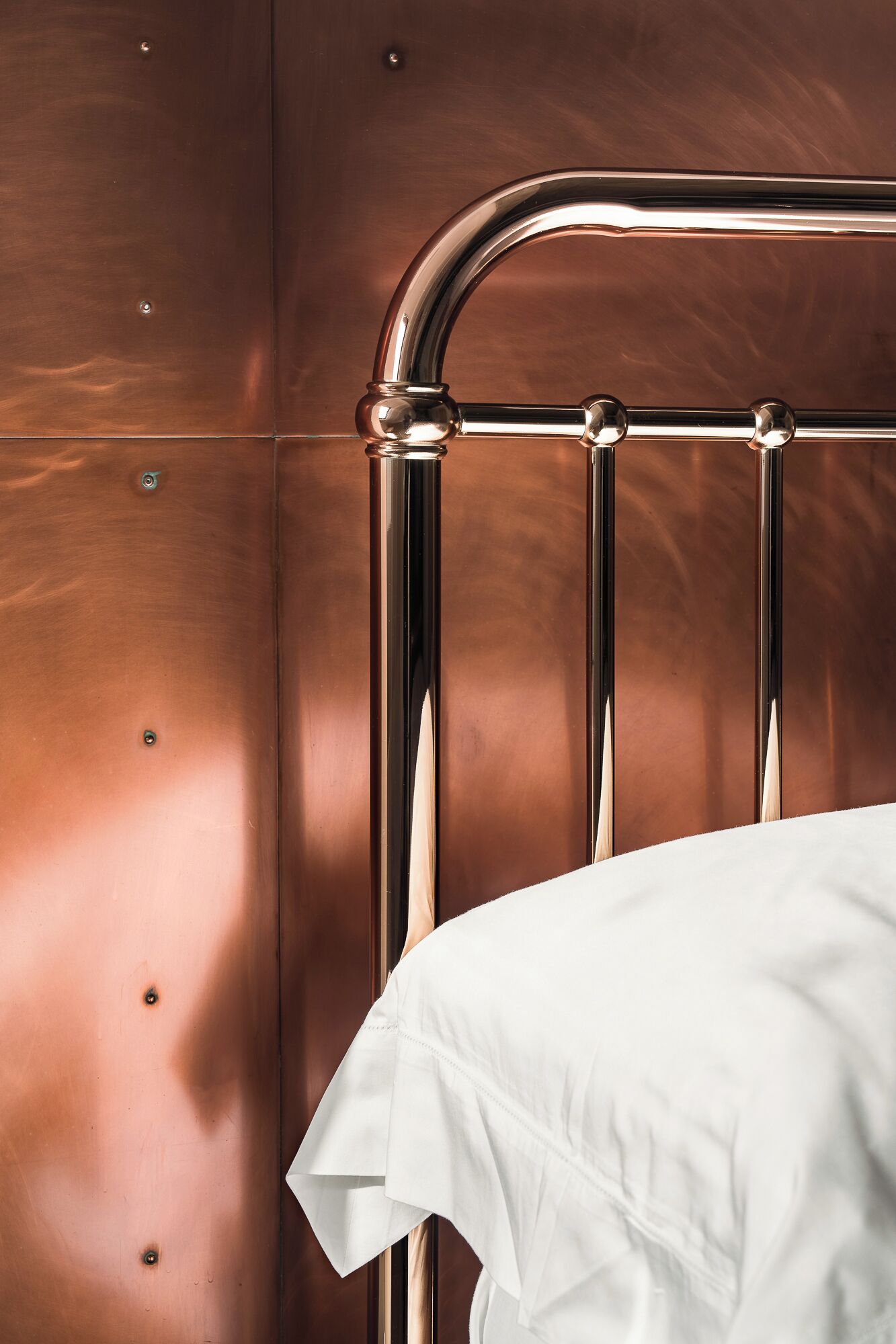 A bed with a metal headboard and a white sheet.