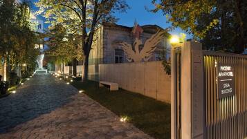 A paved pathway leading to a building with a large tree sculpture and a sign for 'Phoenix Aparthotel' and 'Stela Building'.