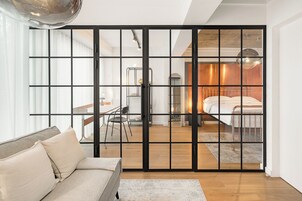 Un interior moderno con una puerta corredera de vidrio que da a un dormitorio con estructura de cama metálica y suelo de madera.