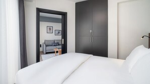 A modern hotel room with a large bed, a dark wardrobe, a small table, and a sofa in the background. - Urban Quarters - Firuzaga (Istanbul)