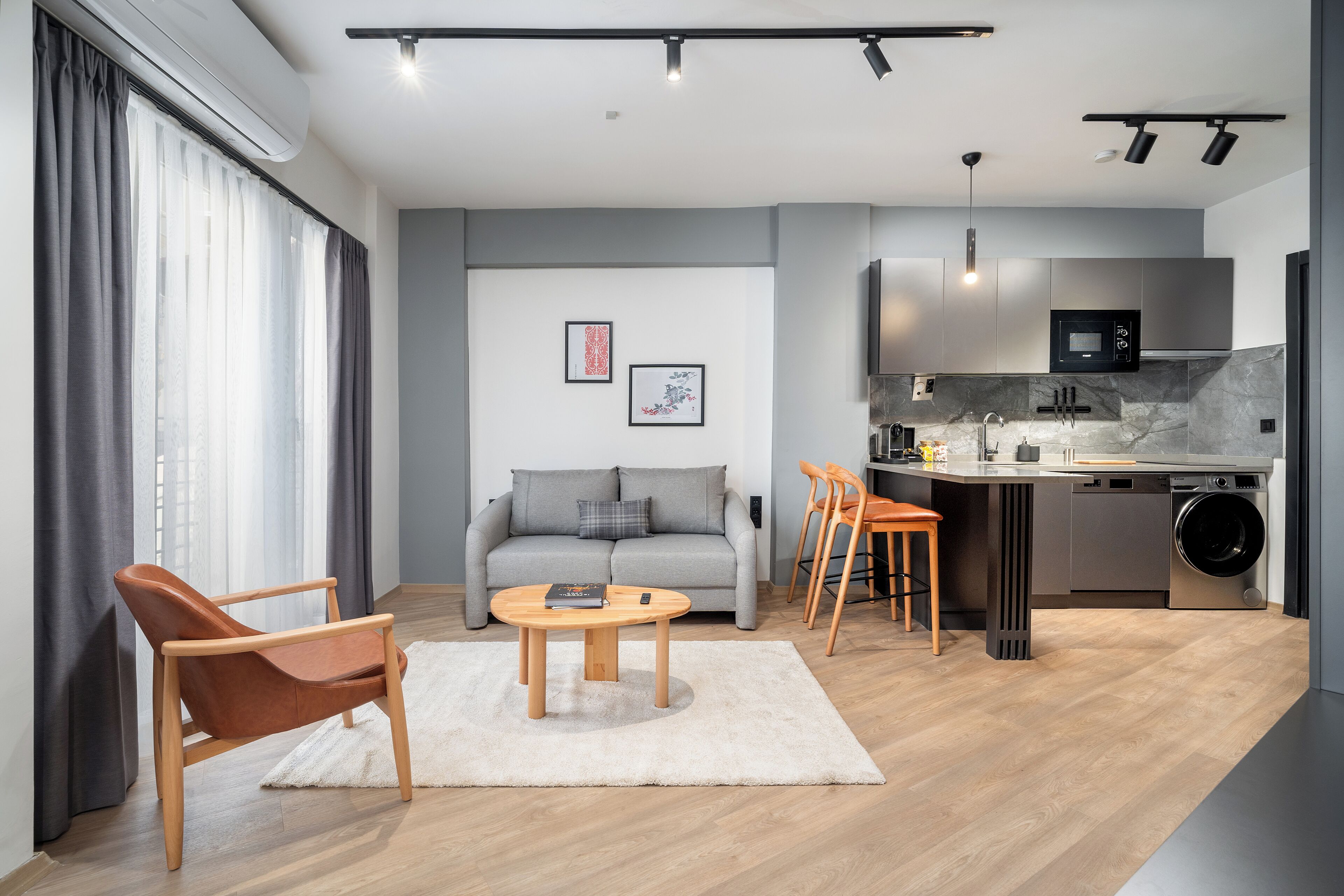 A modern living room with a sofa, coffee table, and chairs, a kitchen with appliances, and a laundry area.