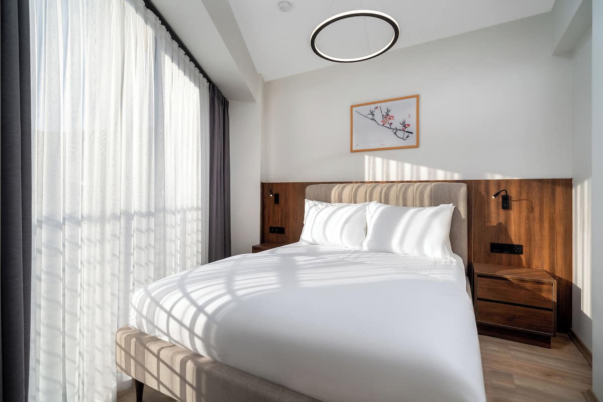 A modern hotel room with a large bed, wooden headboard, two bedside tables, and a framed artwork on the wall.
