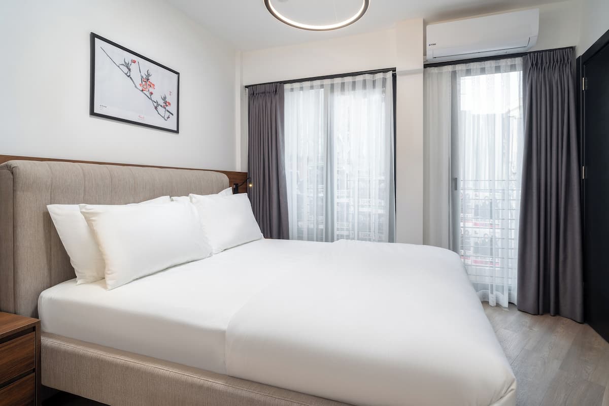 A neatly made bed with white linens, a headboard, and a bedside table with a lamp.