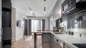 A modern kitchen with a built-in dishwasher, a microwave, and a stove. There is a dining area with a table and chairs. - Urban Quarters - Firuzaga (Istanbul)