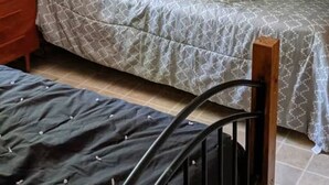 Un lit superposé avec une structure en bois, un lit inférieur recouvert d’une couverture à motifs et un lit simple avec une couverture foncée.