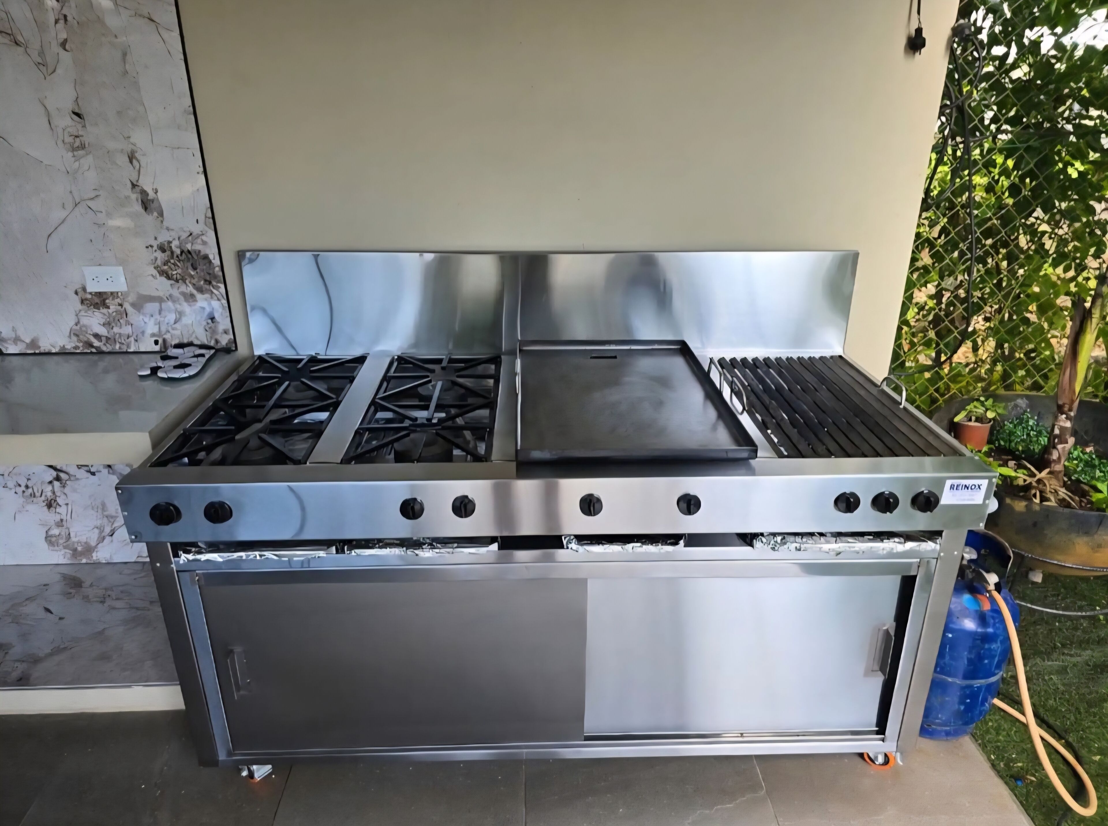 A stainless steel outdoor gas stove with four burners, a built-in oven, and a side compartment.