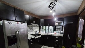 Une cuisine avec des meubles de couleur sombre, un réfrigérateur en acier inoxydable, une cuisinière à gaz et un four à micro-ondes.