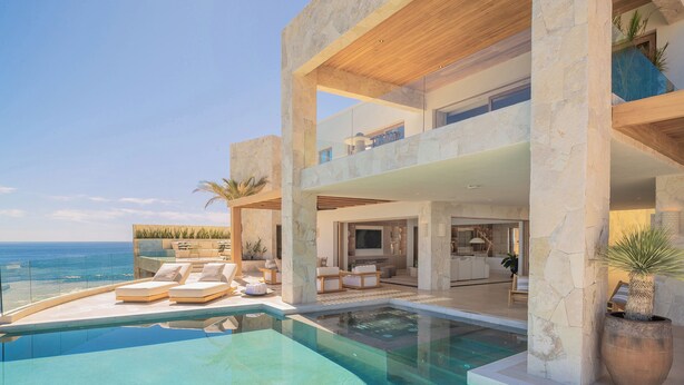 Een modern, meerlaags huis met een zwembad, buitenzitplaatsen en uitzicht op zee.