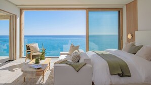 Een moderne slaapkamer met een groot bed, een bank en een stoel, allemaal gericht op een groot raam met uitzicht op de zee.