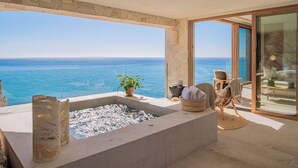 Een modern balkon met een stenen muur, een jacuzzi, rieten meubels en uitzicht op zee.