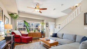 A spacious living room with a ceiling fan, a red armchair, a grey sofa, and a wooden coffee table.